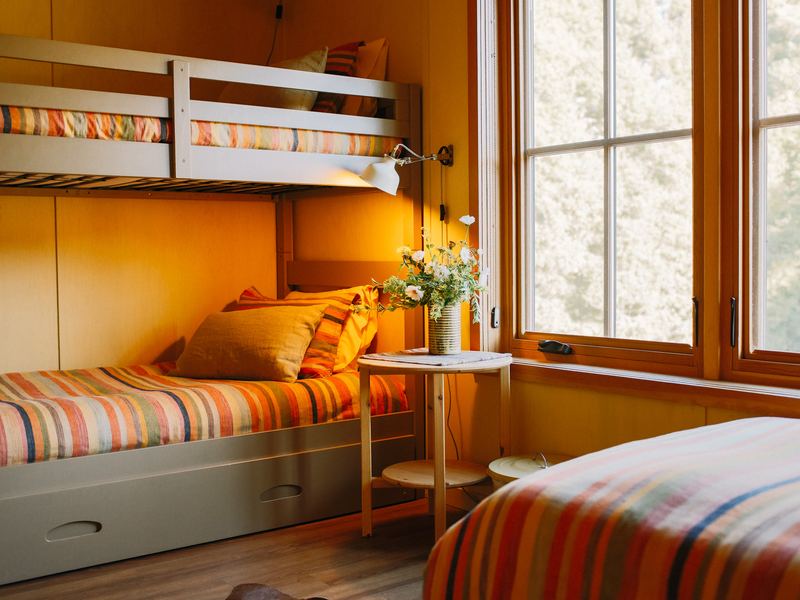 A sunlit room with a bunk bed and a single bed, striped blankets, tall window