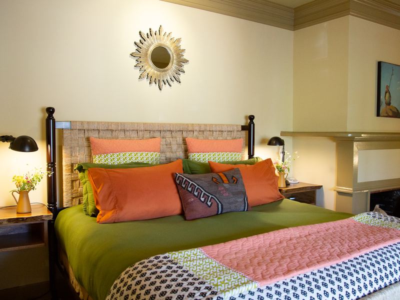 A bedroom with a four-poster bed, green and orange linens, and a fireplace